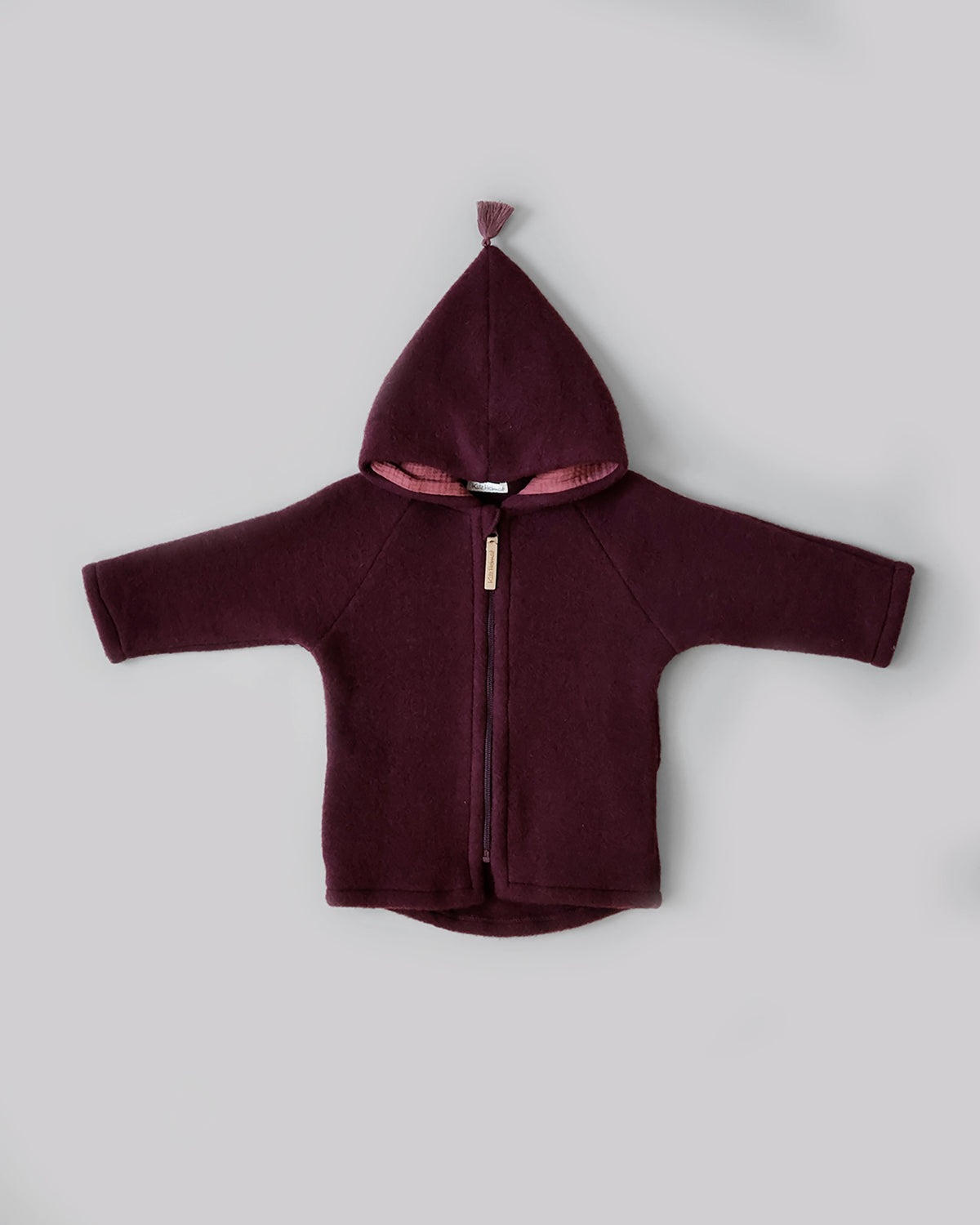 Kitz Heimat Wollfleece-Jacke Burgundy/Burgundy in Vorderansicht mit spitzer Kapuze, rosafarbener Quaste und durchgehendem Reißverschluss.