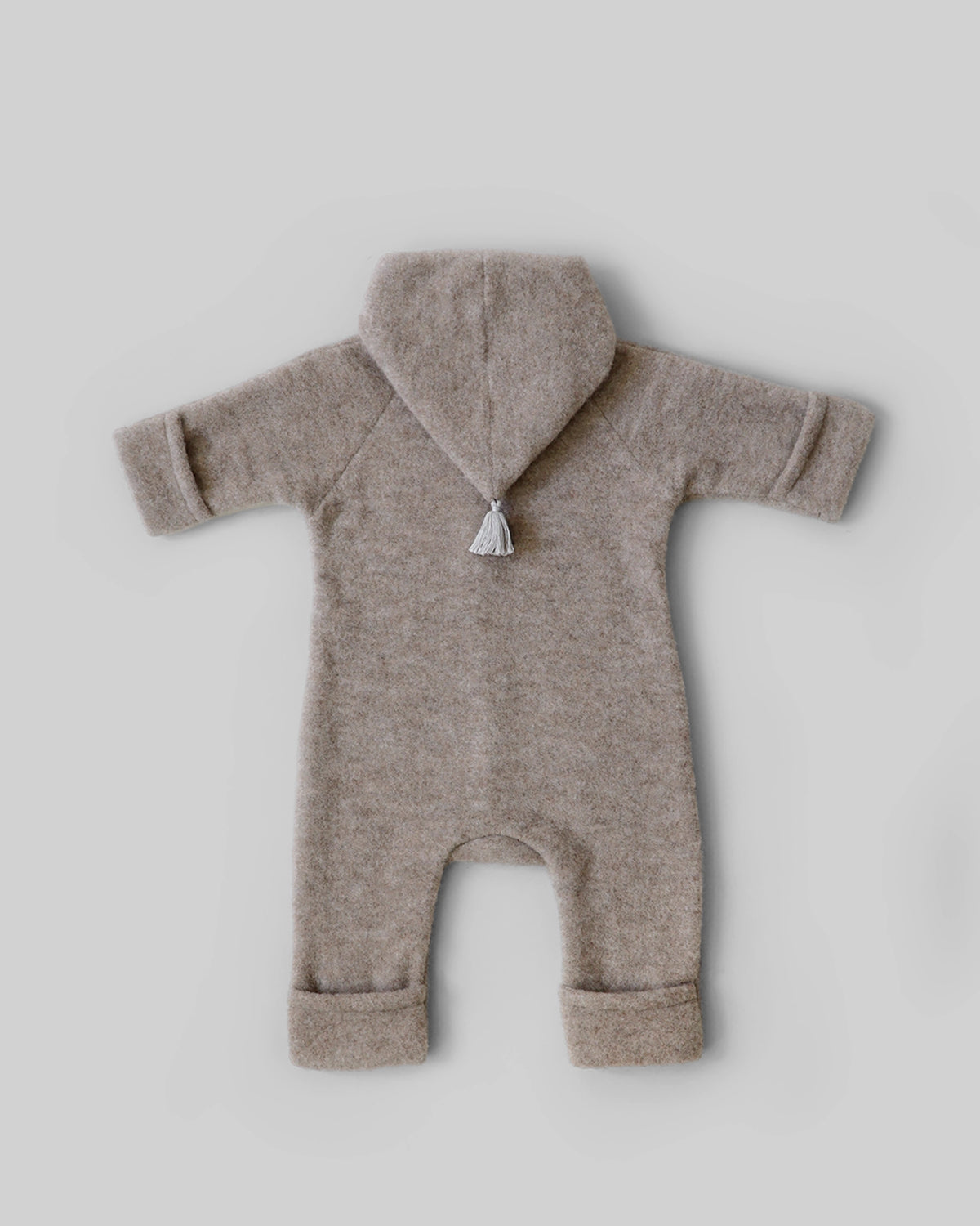 Rückansicht des Kitz Heimat Wollfleece-Overalls in Greige/Nude mit spitzer Kapuze, Quaste und umgeschlagenen Beinabschlüssen.