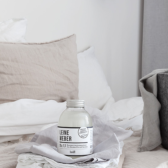 Waschmittelkonzentrat Leineweber in kleiner Flasche auf einem grau weiß bezogenem Bett.