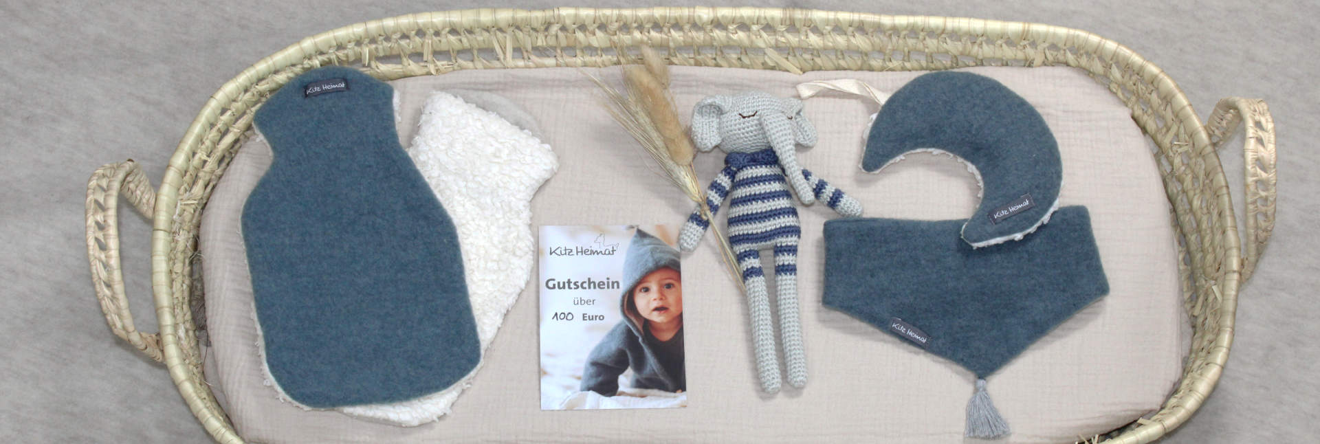 Geschenkideen von Kitzheimat liegen in einem Babykörbchen, wie z.B. Wärmflaschen, Gutschein, Kuscheltier und Wollschal.